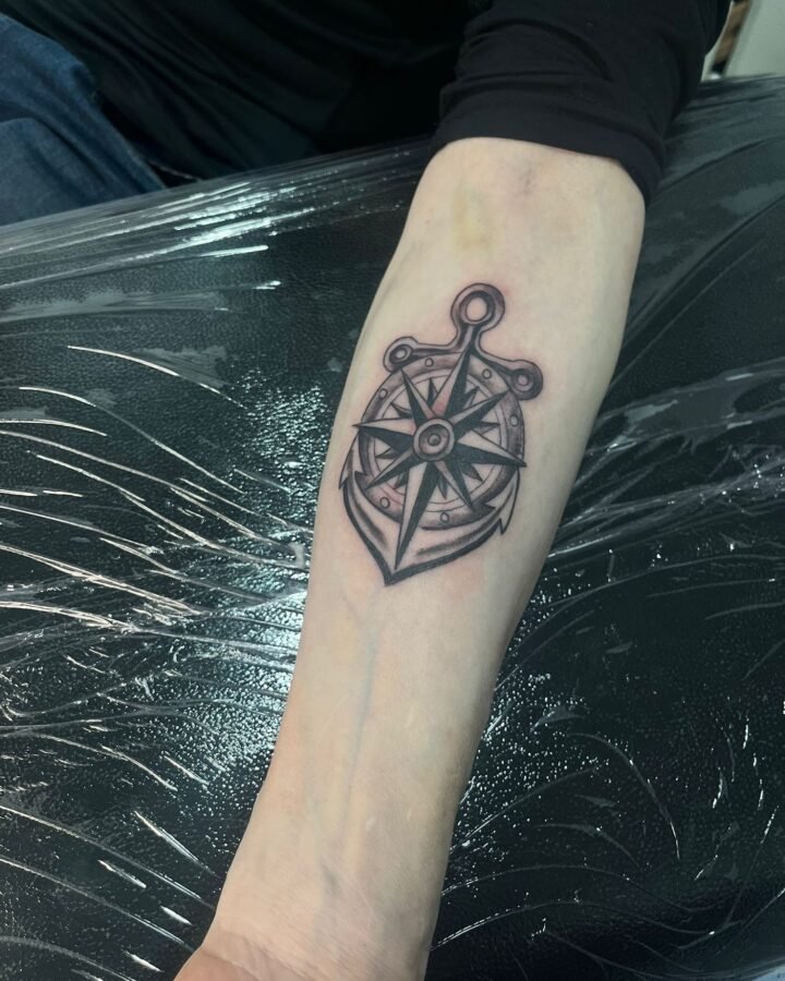 Tatuaje de brújula con ancla en negro en el antebrazo
