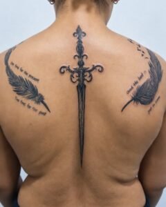 Tatuaje ornamental de daga en la columna con plumas y frases en los omóplatos, por Elena