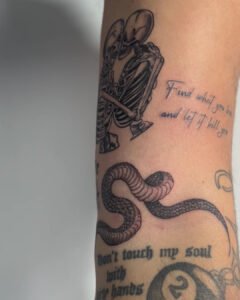 Tatuajes en negro de esqueletos abrazados, serpiente y frase en el brazo